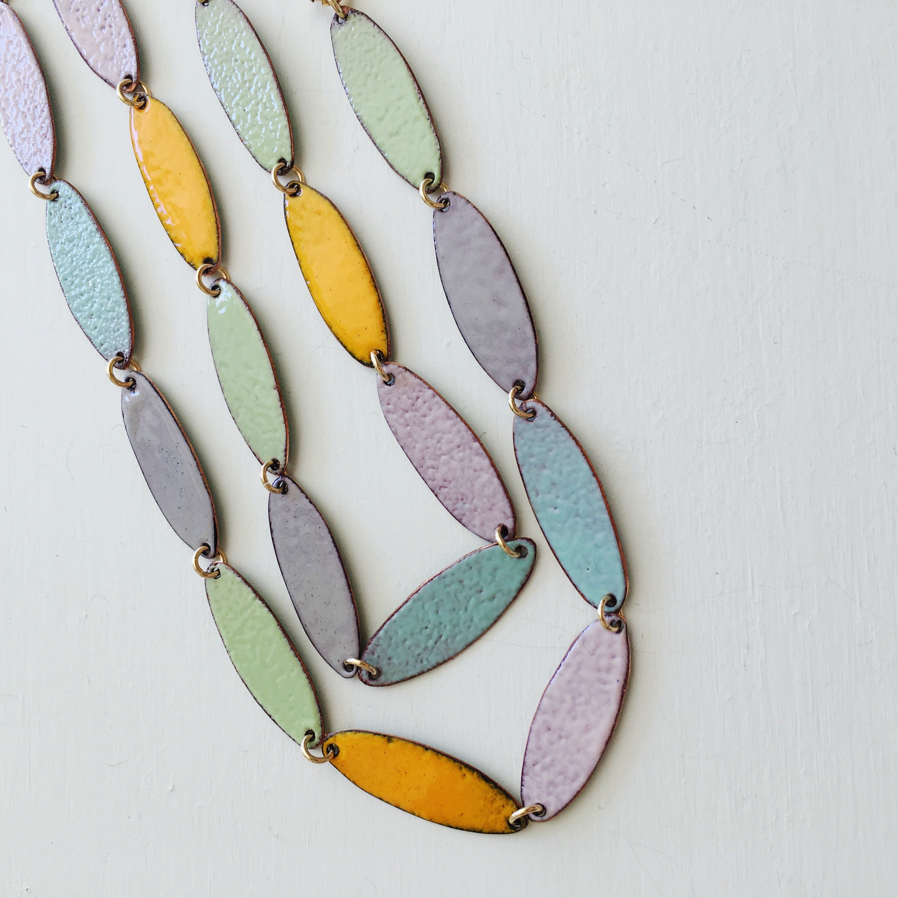 A one of a kind necklace in ellipse shapes of different pastel colors. Each piece is hand cut copper with glass enamel kiln fired on both sides.